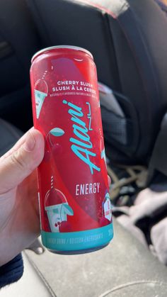 a person holding up a can of energy drink in the back seat of a car