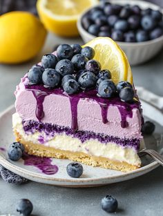 a slice of cheesecake with blueberries and lemons on the side, sitting on a plate