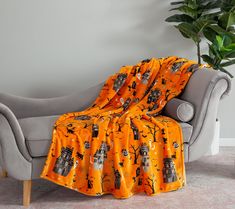 an orange blanket is draped over a grey chair in front of a potted plant