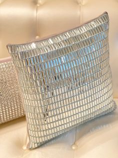 two shiny silver pillows sitting on top of a white leather couch next to each other