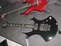 two electric guitars laying on top of a bed next to each other, one red and one black