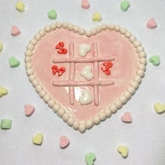 a pink heart shaped cake sitting on top of a white table covered in candy hearts