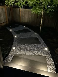 a walkway lit up at night with lights on the ground and trees in the background