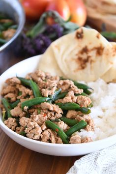 a white bowl filled with meat and green beans on top of rice next to vegetables