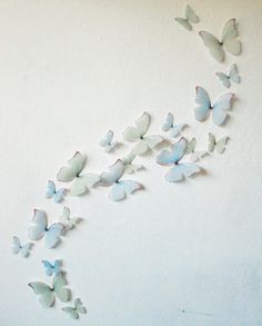 a group of butterflies flying in the air on a white wall with no one around them