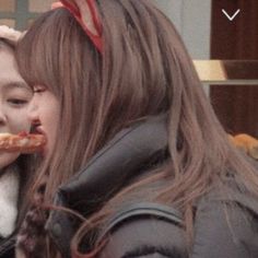 two girls are eating pizza outside on the street and one girl is wearing a red bow around her head