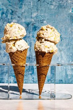 two cones of ice cream sitting in front of a blue wall and glass stand with one cone full of ice cream