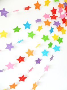 multicolored paper stars are arranged on a white surface, with one falling off the wall