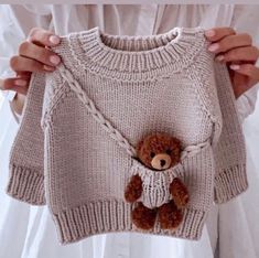 a person holding up a sweater with a teddy bear attached to the front and bottom