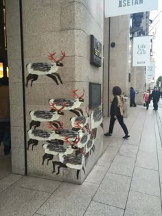 a woman walking down a sidewalk past a tall building with paintings on the side of it