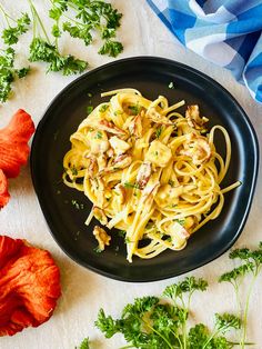 a black plate topped with pasta and parsley on top of a white tablecloth