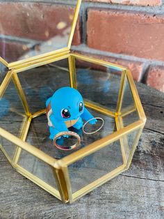 a small blue toy in a glass box on top of a wooden table next to a brick wall