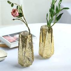 two vases with flowers are sitting on a table next to each other and one is empty