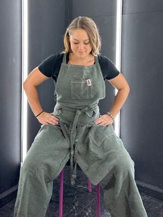 a woman sitting on a stool with her hands on her hips wearing an apron and overalls