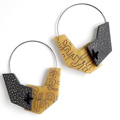 two metal hoop earrings with black and gold designs on them, one has a bow