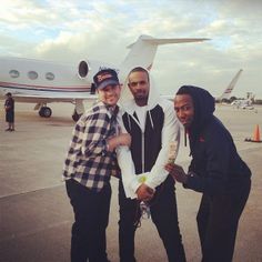 three people standing in front of an airplane on the tarmac with one person holding something