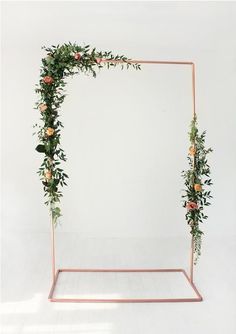 a pink metal frame with flowers and greenery on the top is against a white wall