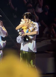 two people holding stuffed animals in their arms on stage with an audience watching them from the stands