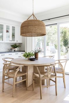 a dining room table with chairs and a basket hanging from it's ceiling in front of large windows