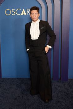 a man in a tuxedo poses for the camera at an oscars event