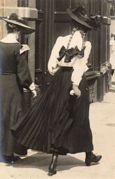 an old black and white photo of two women in long dresses with hats on their heads