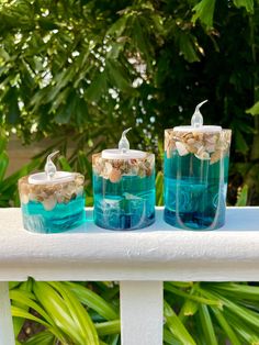 three blue candles sitting on top of a white table next to some plants and trees