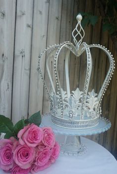 a white cake topped with a crown on top of a table next to pink roses