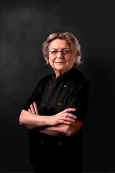 an older woman with glasses and a black shirt is posing for a photo in front of a dark background