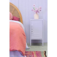 a small white cabinet next to a bed in a room with purple walls and pink bedspread