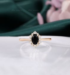 a black diamond ring sitting on top of a white table next to a pink flower