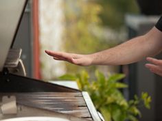 a person holding out their hand to another person on a grill outside with trees in the background