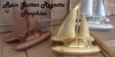 three small sailboats sitting on top of a wooden floor next to each other with the words rain gutter regatta trophies above them