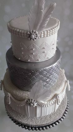 three tiered wedding cake with white frosting and feathers on top, decorated with beading