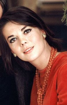 a close up of a person wearing an orange shirt and pearls on her necklaces