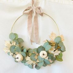 a wreath with leaves and flowers hanging on a white cloth covered wall, next to a beige ribbon