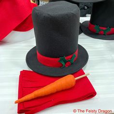 two hats and a carrot sitting on top of a white tablecloth covered table with red napkins