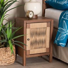 a nightstand with a clock on it next to a bed and plants in a basket