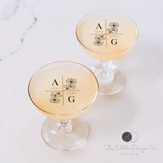 two wine glasses sitting on top of a table with the letters a and g in them