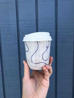 a hand holding up a cup that is painted with blue and white designs on it