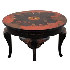 an orange and black table with flowers painted on the top, sitting in front of a white background