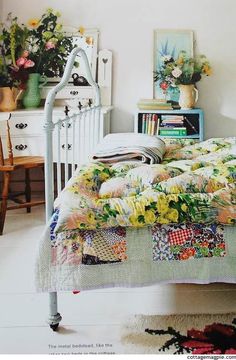 a white bed topped with lots of pillows next to a dresser and table filled with flowers