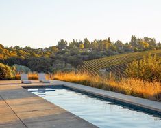 an empty swimming pool in the middle of a field with trees and bushes behind it