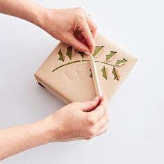 a woman is wrapping a present in brown paper with green leaves on it and holding a wooden stick