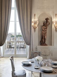 a dining room table set with place settings and plates on it, in front of a large window