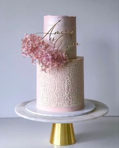 a pink and white wedding cake with flowers on the top is sitting on a gold pedestal