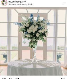 a vase with white and blue flowers sitting on a table in front of a window