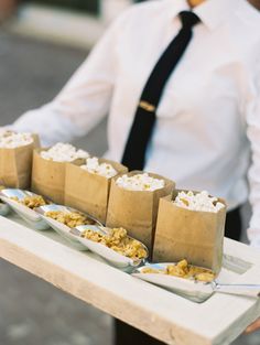 a man in a tie holding a tray with desserts on it and paper bags