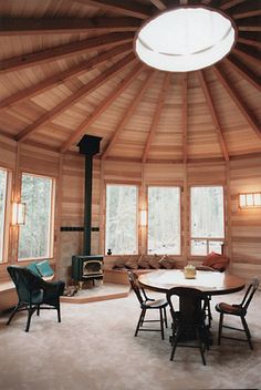 the inside of a wooden cabin with round table and chairs in front of an open fire place