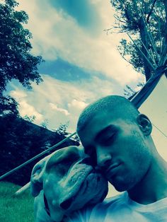 a man holding a dog in his arms while sitting on the grass near a tree