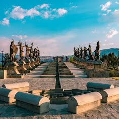 the statues are lined up in rows on the stone walkways with blue sky and clouds behind them